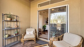 Ein gemütlicher Patio-Bereich mit Korbmöbeln, einem Metallregal mit Pflanzen und einer Glastür, die zu einem Innenbereich führt.