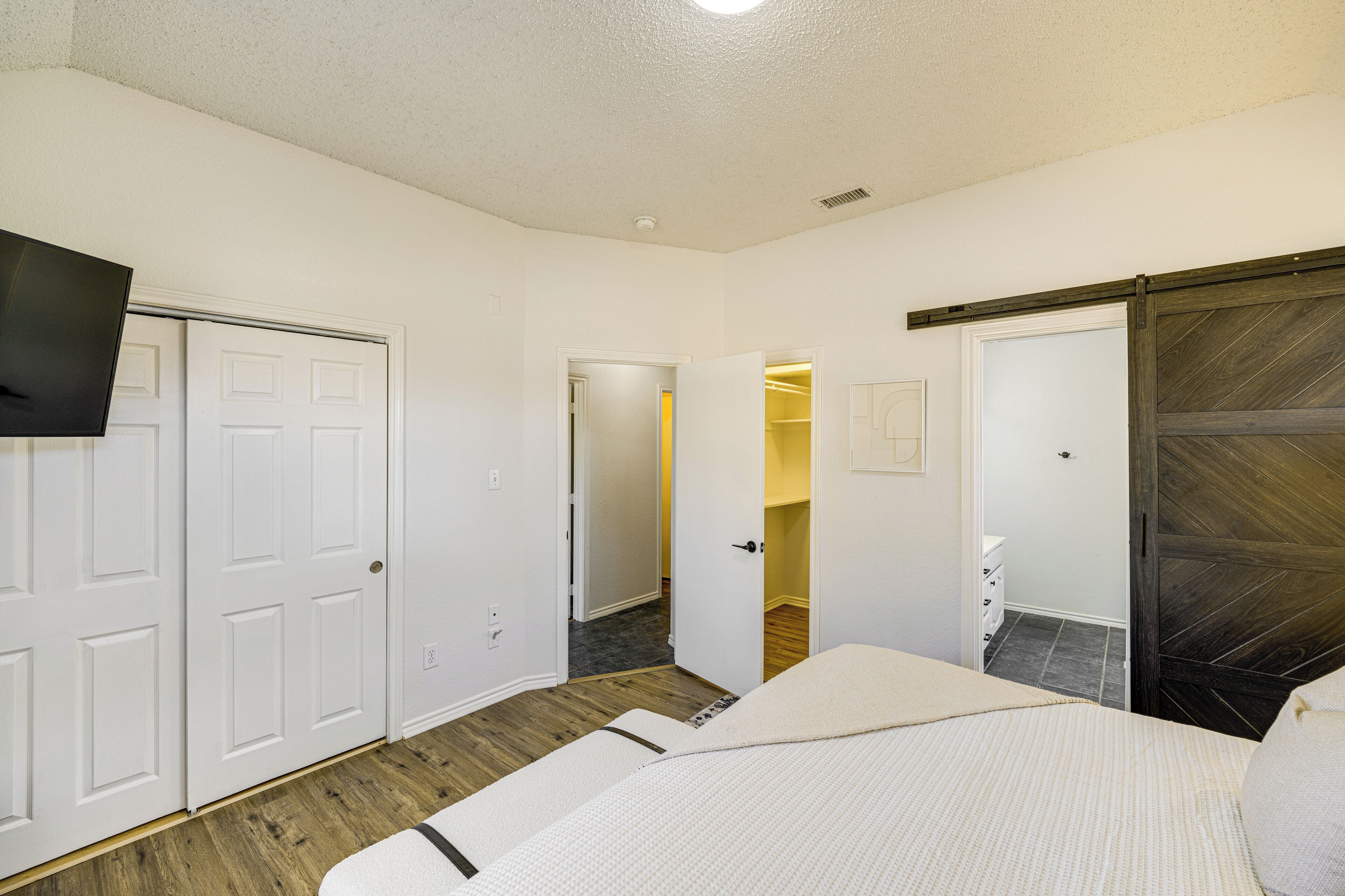 Une chambre à coucher avec un lit, une télévision, une armoire et une salle de bain visible à travers une porte ouverte.
