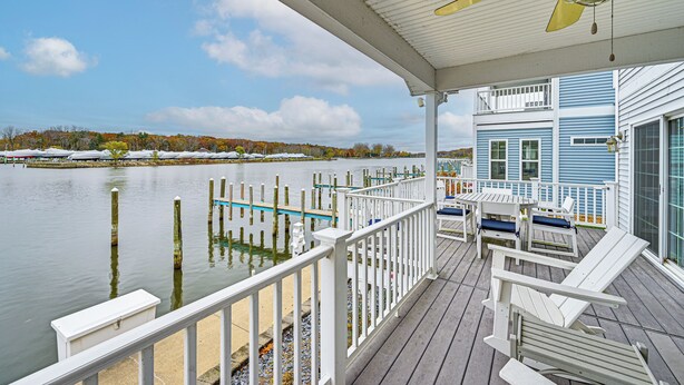 A covered deck with white railings, a ceiling fan, and a view of a lake with dock posts. - St Joseph River, Lake Michigan Access: Luxury Home (Saint Joseph)