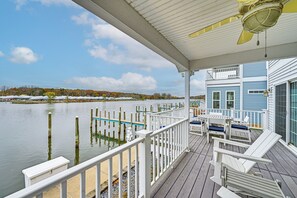 Une terrasse couverte avec des rampes blanches, un ventilateur de plafond et une vue sur un lac avec des piliers de quai.