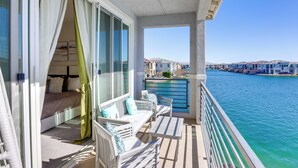 A balcony with white furniture, a bed with a green curtain, and a view of a marina with boats and buildings. - Lake & Mountain Views: Indio Oasis w/ Pool (Indio)