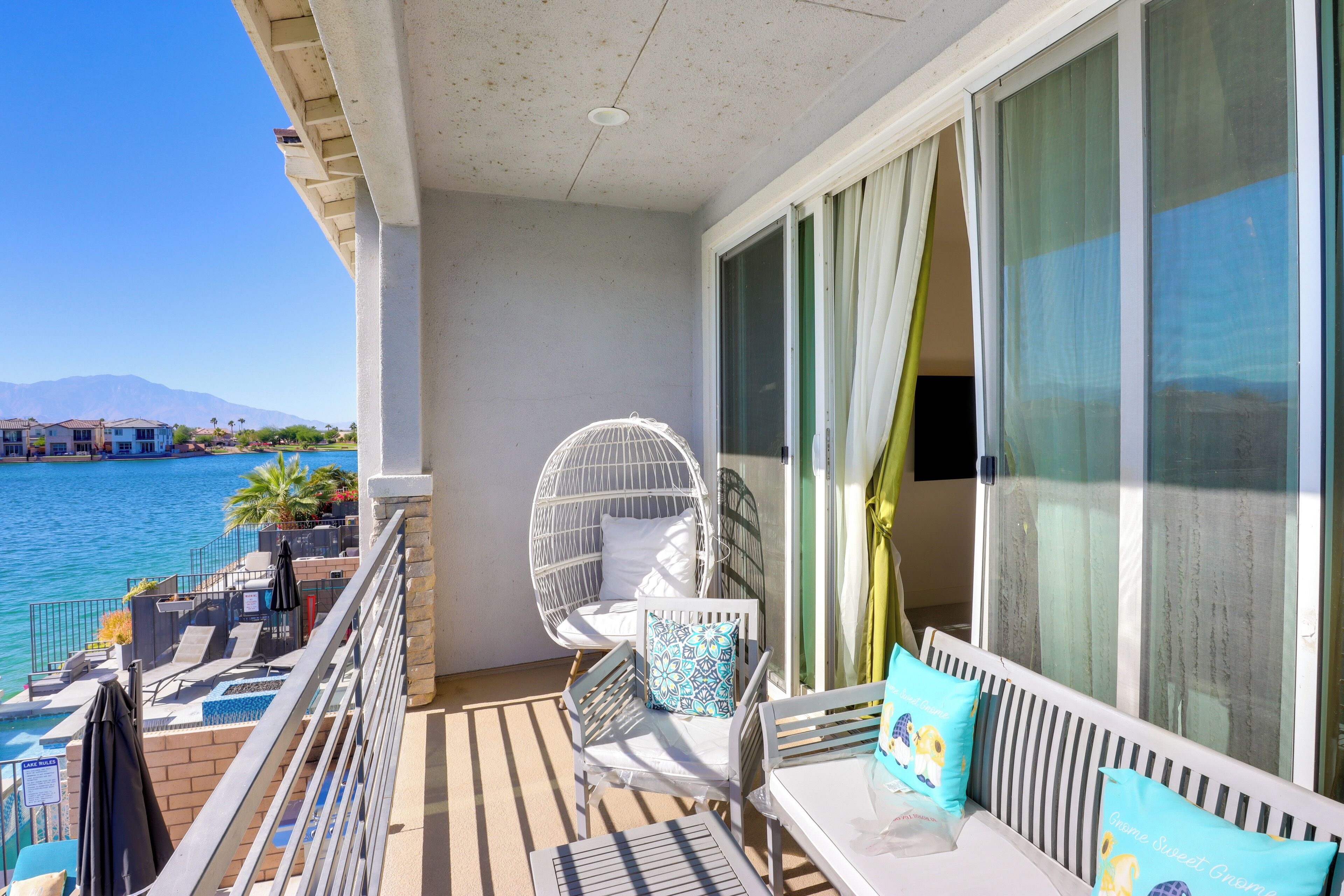 Un balcon avec vue sur la mer, une chaise blanche, un canapé avec des coussins et une table.