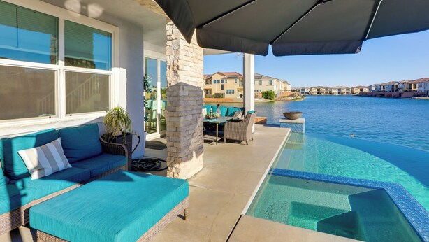 An infinity pool with a clear view of the water, a wicker sofa with teal cushions, and a stone pillar. - Lake & Mountain Views: Indio Oasis w/ Pool (Indio)