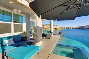 En infinitypool med fri utsikt över vattnet, en soffa av rotting med turkosa kuddar och en pelare av sten.