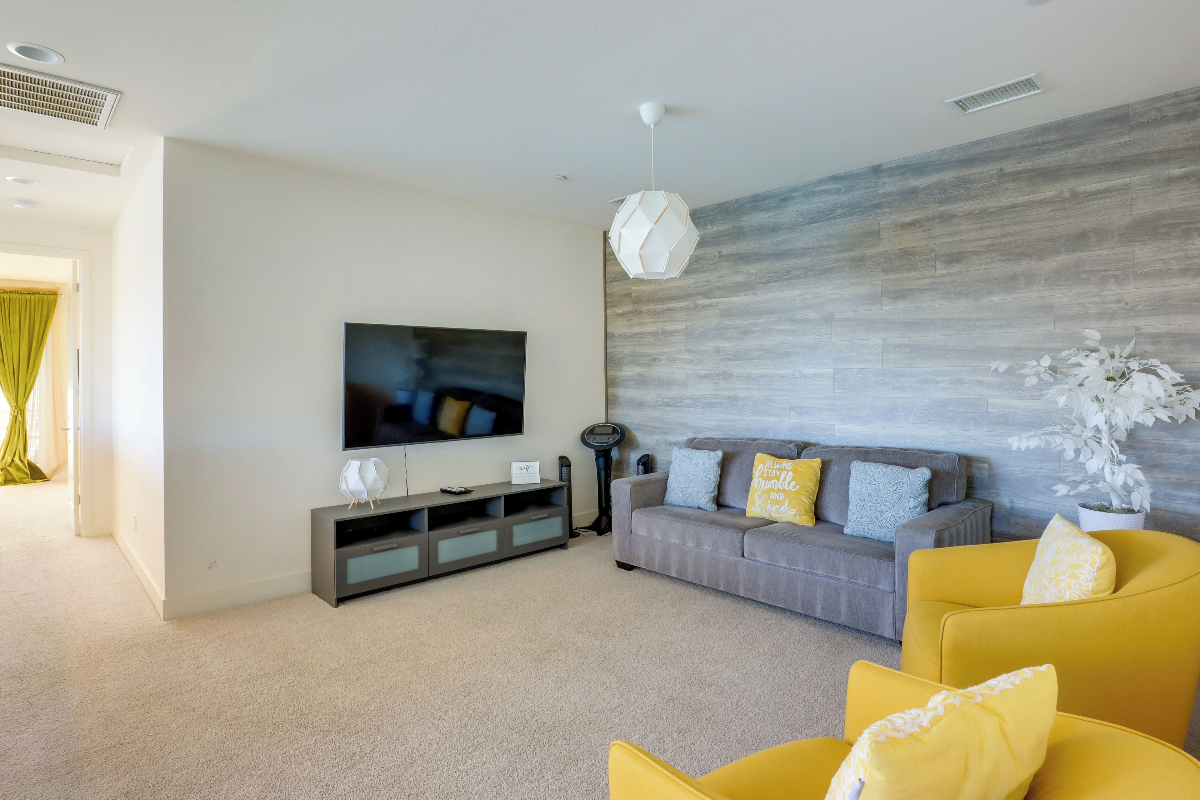 A modern living room with a grey sofa, yellow armchairs, a flat-screen TV, and a decorative wall.