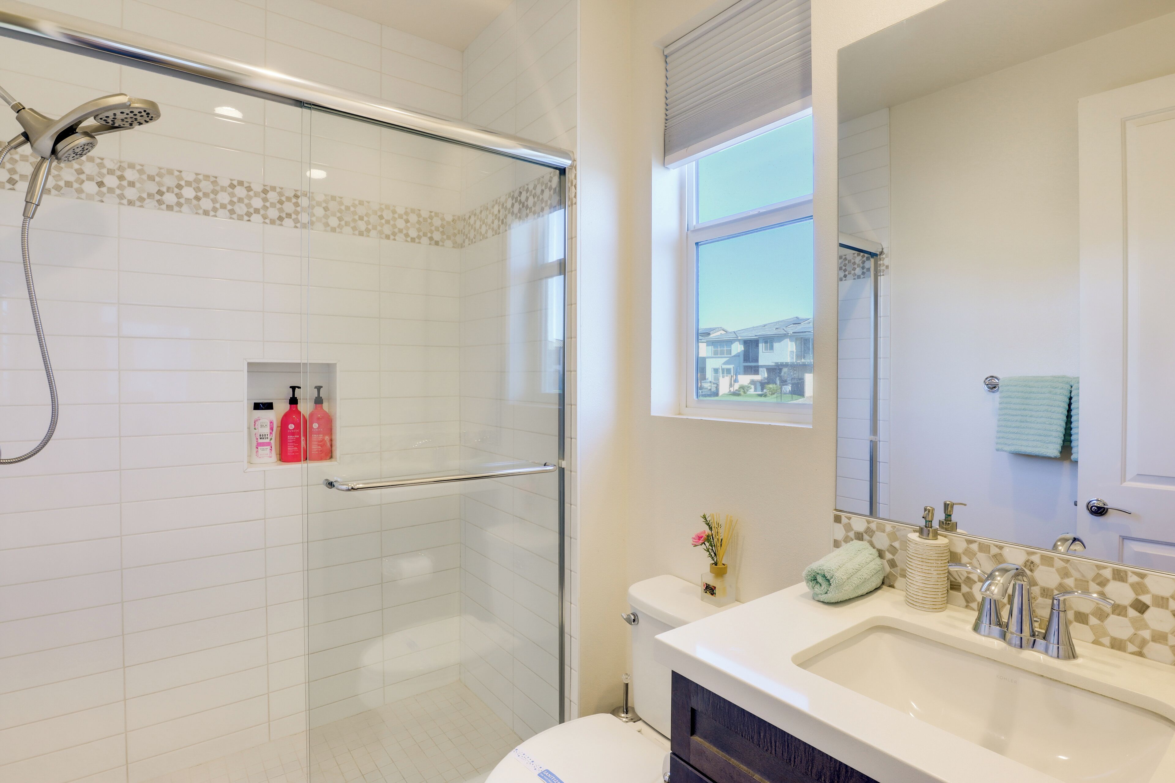 A modern bathroom with a glass shower enclosure, a toilet, a sink with a mirror, and a window providing a view of the outside.