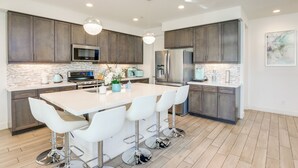 A modern kitchen with dark cabinets, a large island with bar stools, stainless steel appliances, and a tiled backsplash. - Lake & Mountain Views: Indio Oasis w/ Pool (Indio)