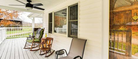 A covered porch with rocking chairs and a ceiling fan.