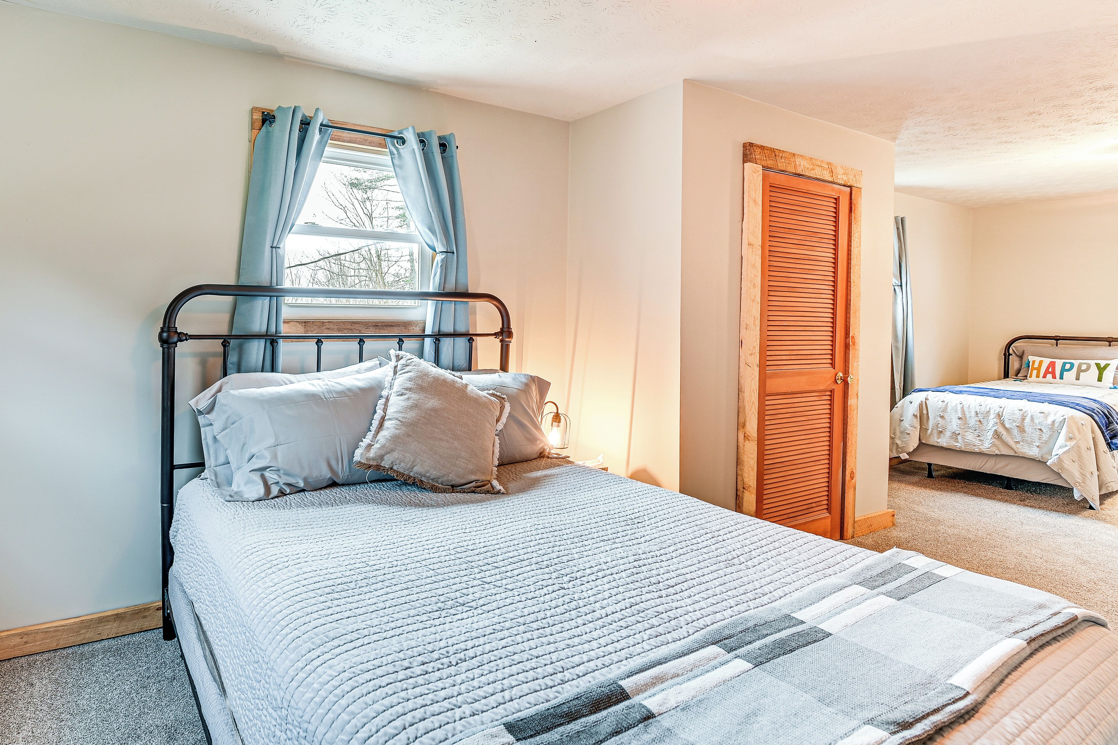 Une chambre à coucher avec un lit, une fenêtre avec des rideaux, une porte en bois et un deuxième lit à l’arrière-plan.