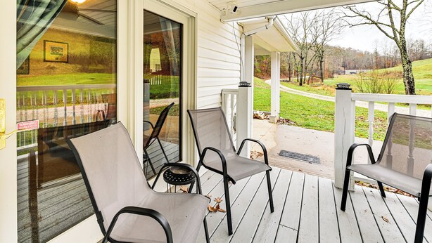 A covered porch with two chairs and a table, overlooking a grassy area with trees and a pathway. - On 220 Acres: Home w/ Trails in West Liberty! (West Liberty)