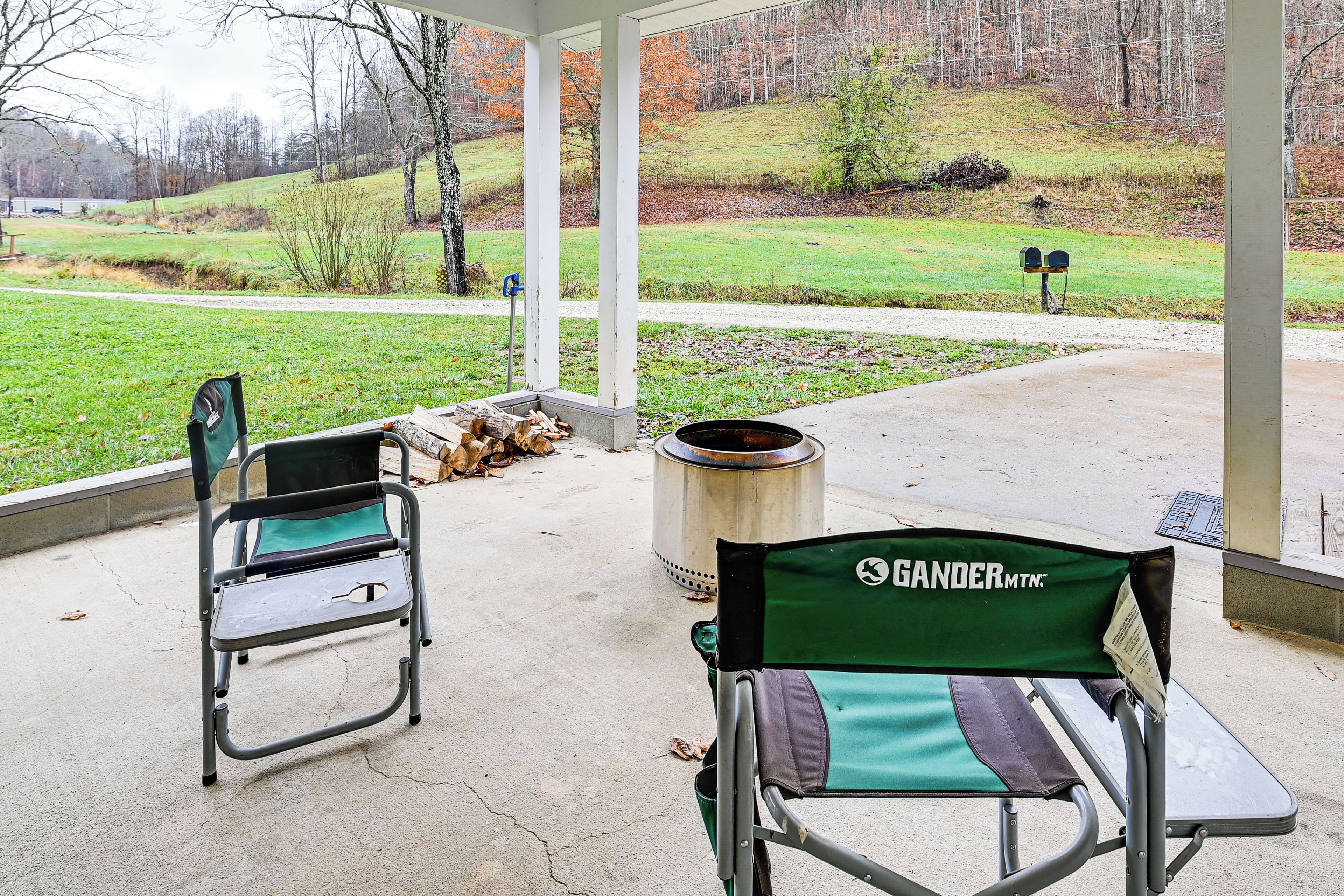 A covered patio area with two green folding chairs, a metal trash can, and a metal table.