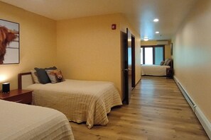 Ein Hotelzimmer mit zwei Betten, einem Nachttisch, einem gerahmten Bild an der Wand und einer Tür zu einem weiteren Raum.