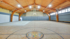 Una cancha de baloncesto en el interior, con techo de madera y aro central.