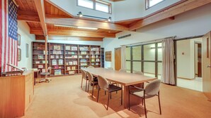 Una habitación espaciosa con una larga mesa y sillas, una estantería llena de libros y un gran ventanal con cortinas.