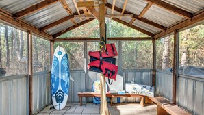 A covered outdoor area with a wooden bench, a surfboard, and a kayak.