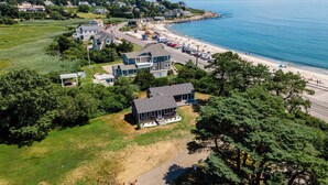 An aerial view of a coastal property with multiple houses, a beach, and a road leading to the shore. - Steps to North Hampton Beach: Cottage w/ Deck! (North Hampton)