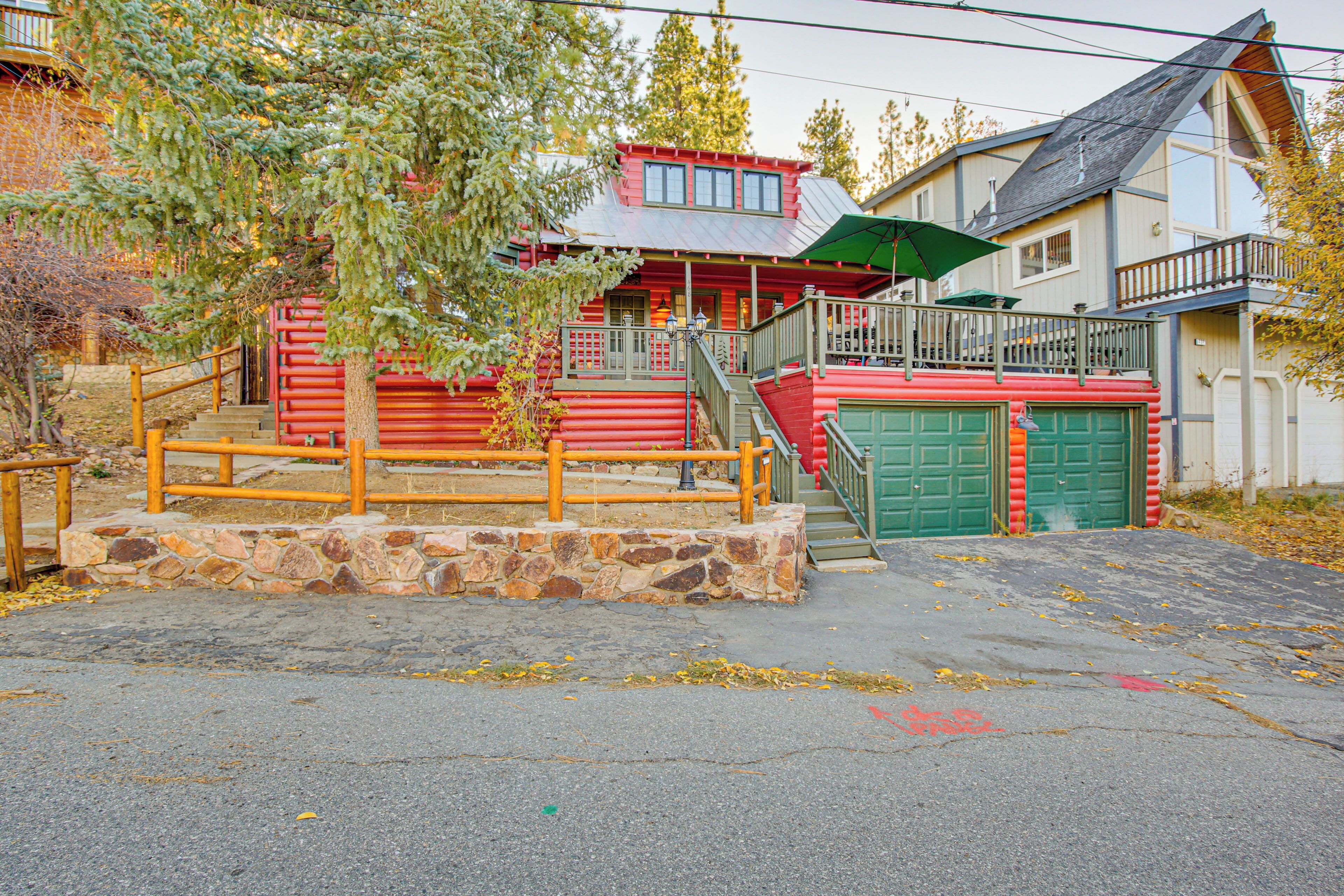 A red log cabin with a stone staircase, a green garage, and a balcony overlooking the driveway.