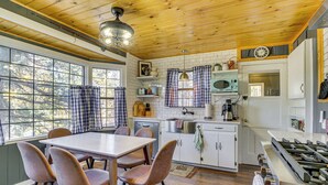 A kitchen with a wooden ceiling, white cabinets, a dining table with chairs, a microwave, and a stove.