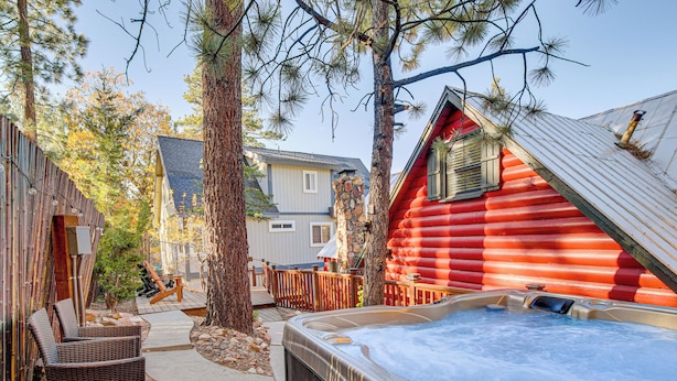 A hot tub in a backyard with a wooden deck and a red cabin.