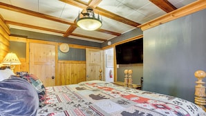 A cozy room with a large bed, wooden ceiling beams, a wooden door, and a wall-mounted TV.