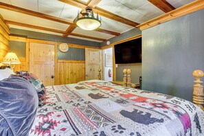 Um quarto acolhedor com uma cama grande, vigas de madeira no teto, uma porta de madeira e uma TV fixada na parede.
