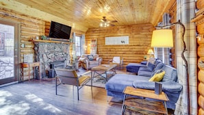 A log cabin interior with a stone fireplace, wooden furniture, and a television mounted on the wall.