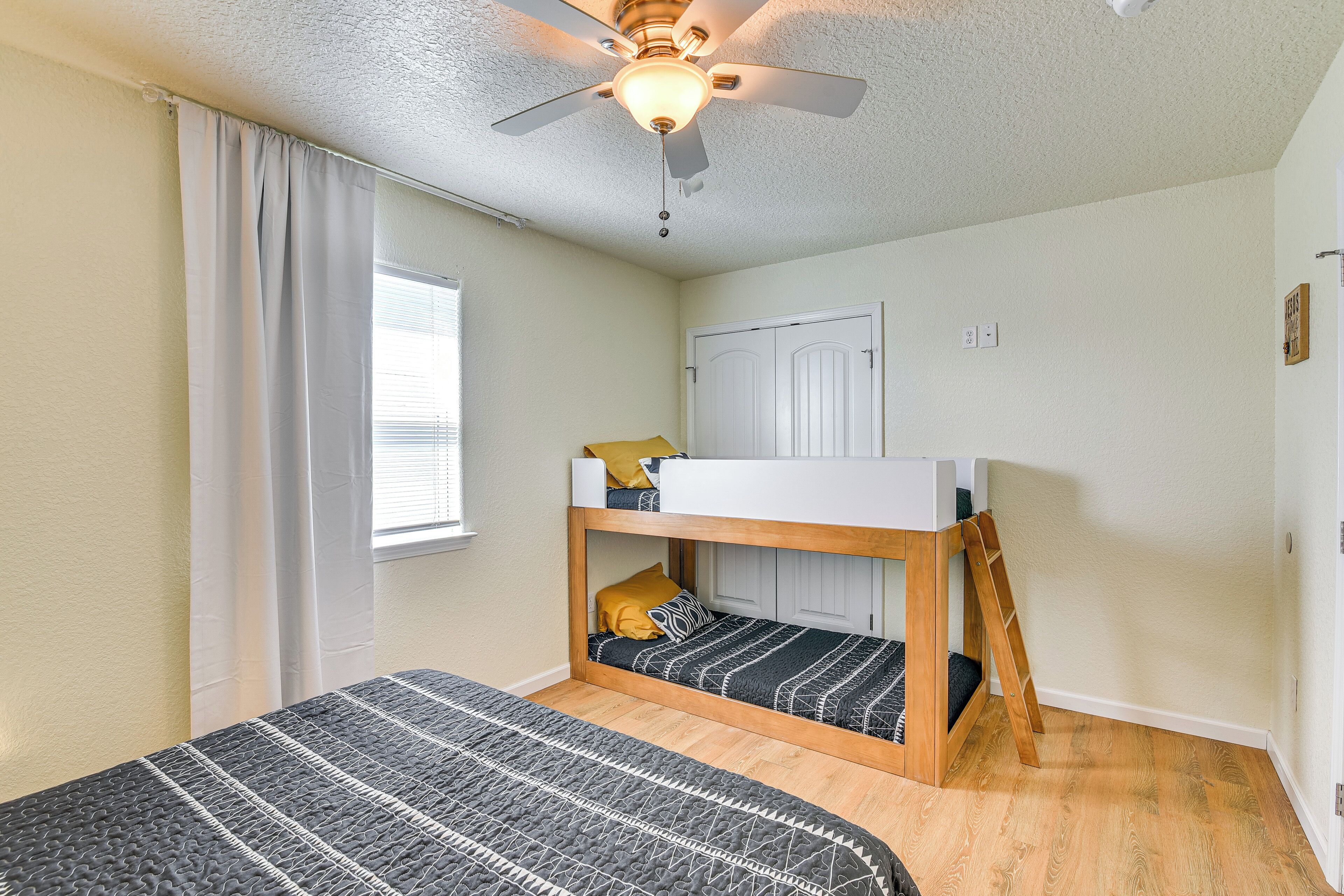 A room with a bunk bed, a ceiling fan, and a window with curtains.