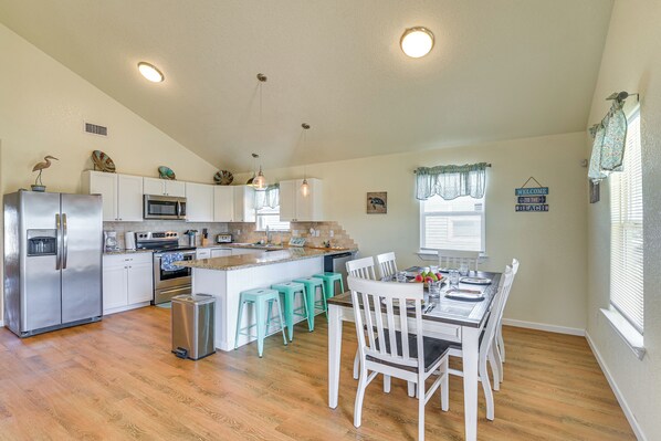 A kitchen with white cabinets, a stainless steel refrigerator, a microwave, and a sink. There are turquoise stools and a dining table with chairs. - Walk to Beach: Gulf-view Home in Surfside Beach! (Freeport)