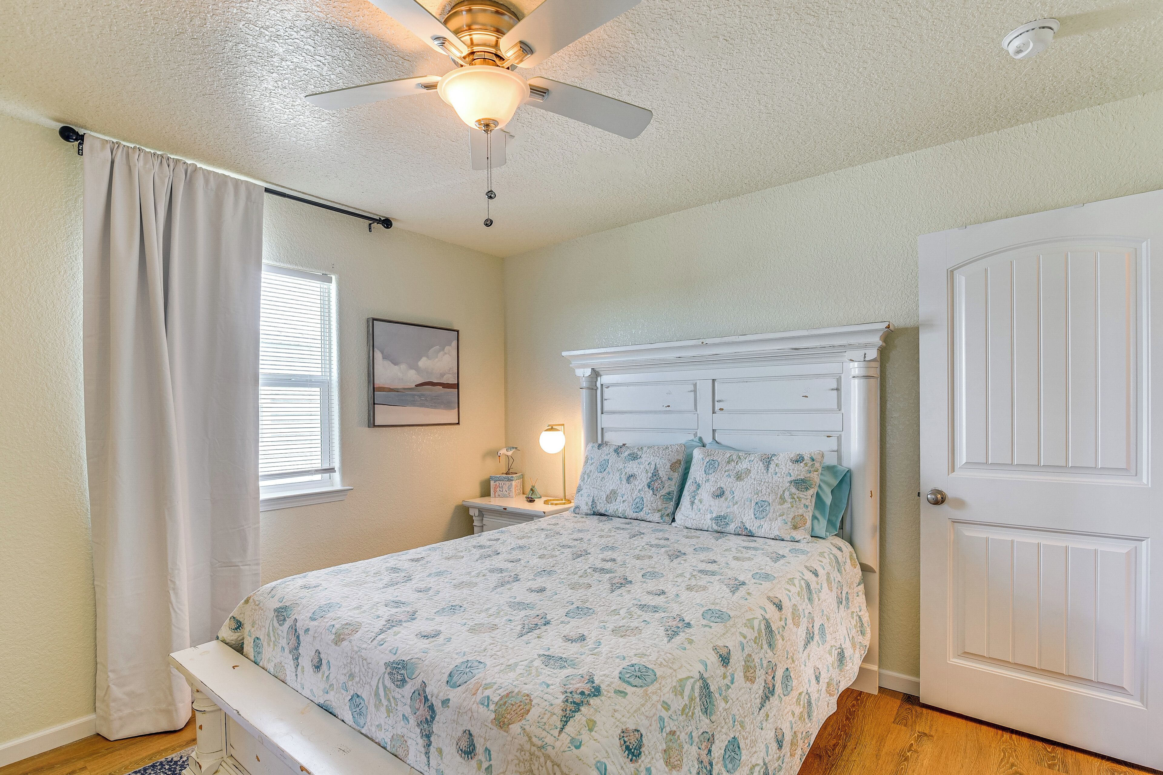 A bedroom with a bed, a ceiling fan, a nightstand, a lamp, and a door.