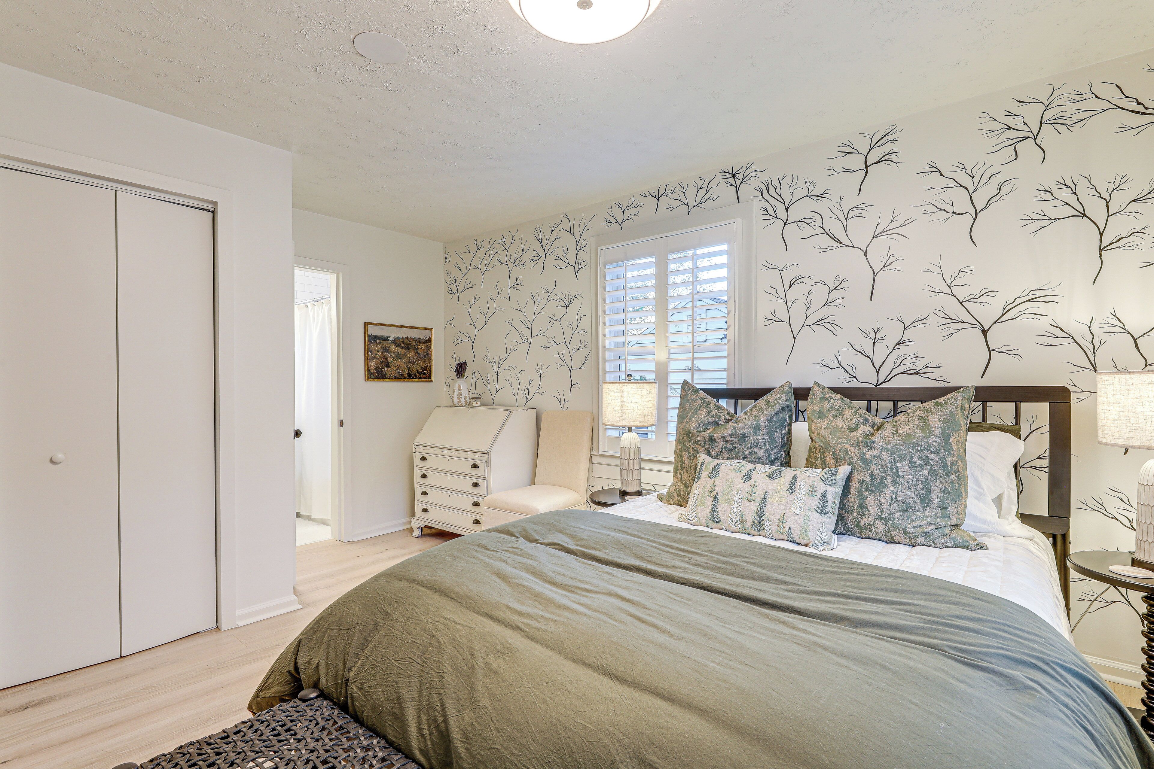 Une chambre à coucher avec un lit, une commode, une chaise et une fenêtre avec des stores.