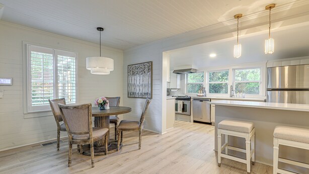 A modern kitchen with white cabinetry, stainless steel appliances, and a dining area with wooden chairs and a round table. - Walk Downtown & Canton Street: Roswell Retreat! (Roswell)