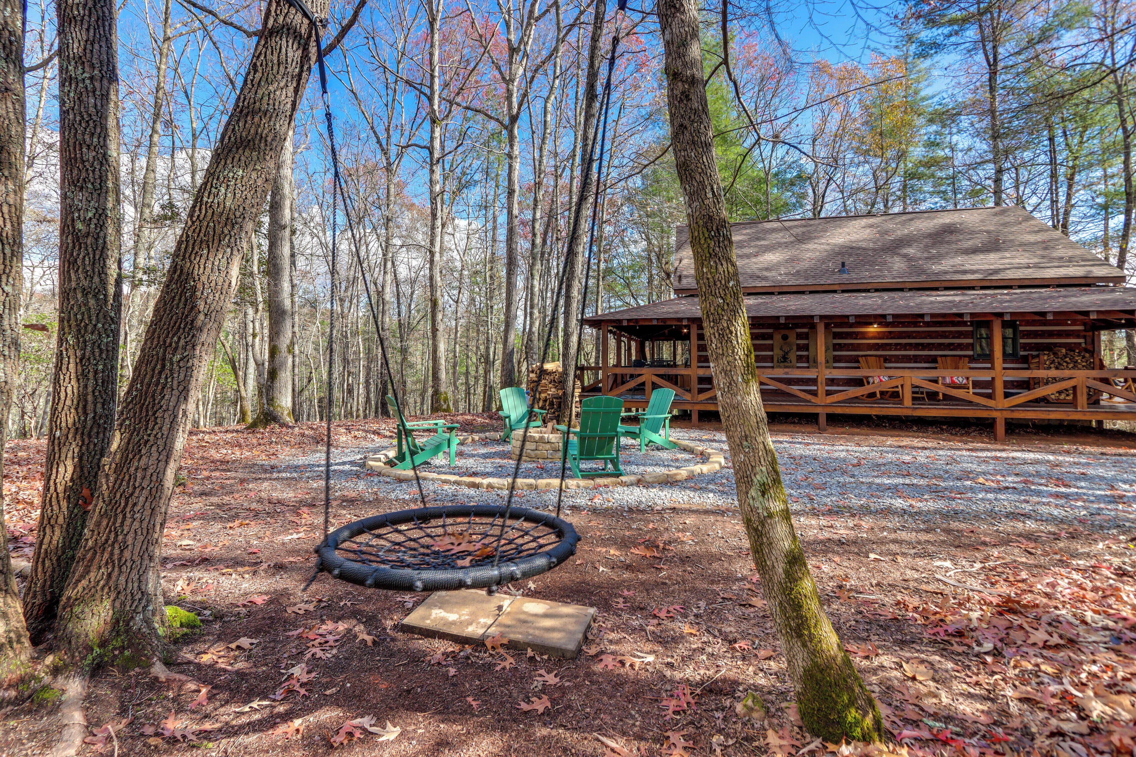 A wooden cabin with a swing set and outdoor seating area surrounded by trees.
