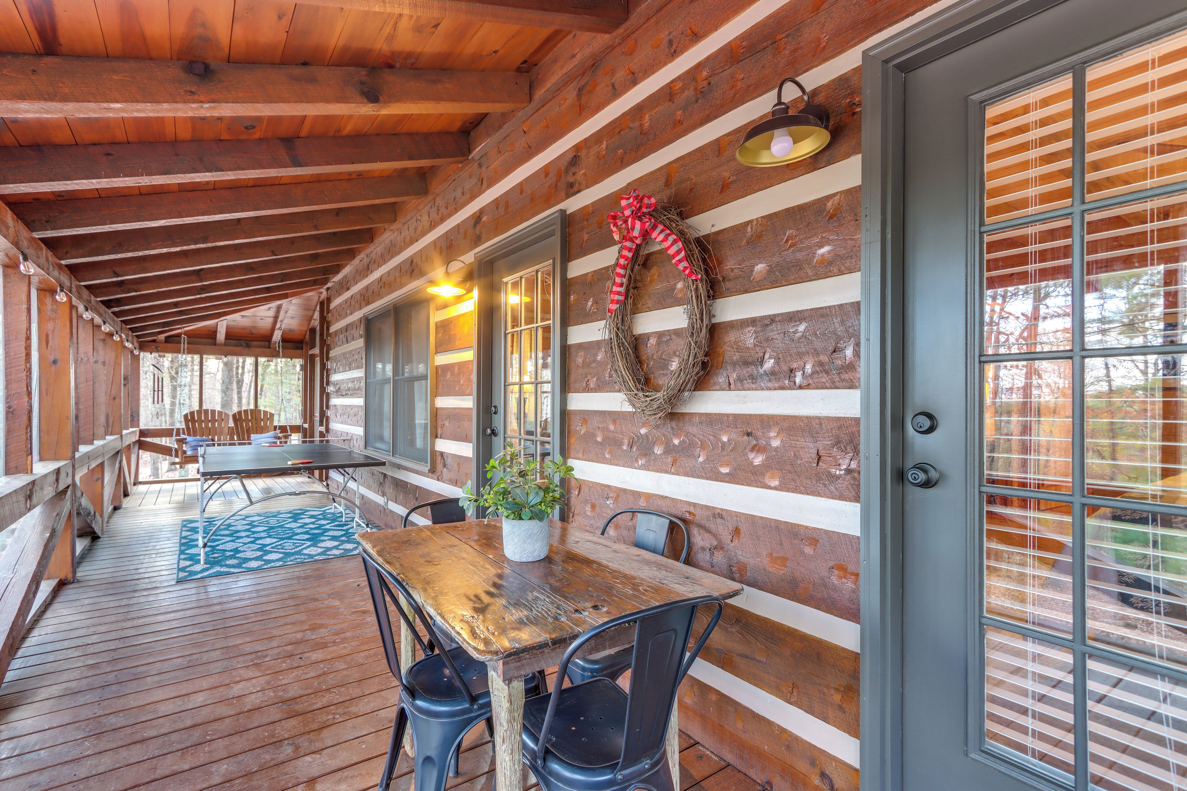 A wooden cabin with a covered porch, a dining table with chairs, and a wreath on the wall.