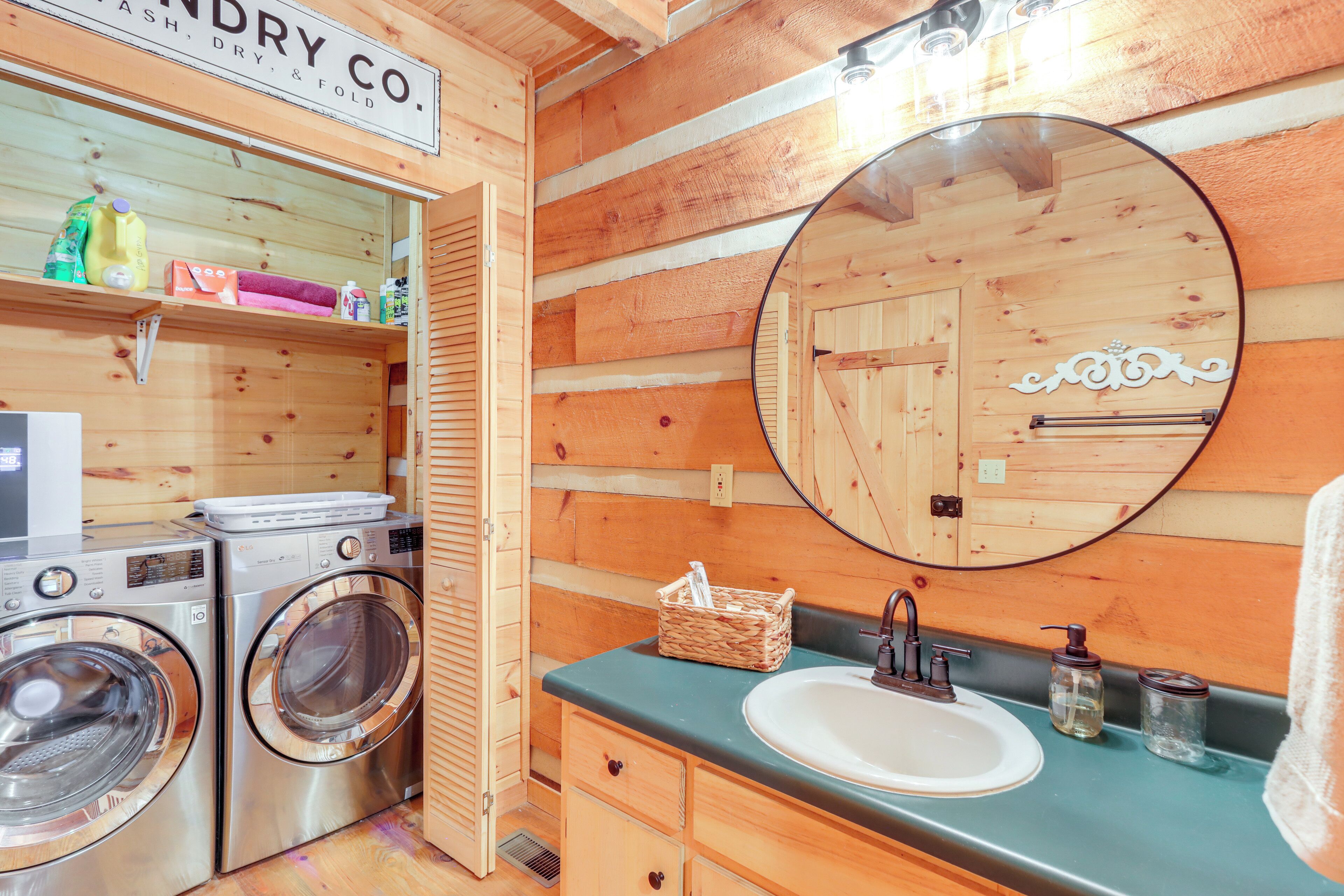 Ein Waschraum mit zwei Edelstahl-Waschmaschinen und -Trocknern, einem Waschbecken mit Spiegel darüber und einer Holzwand mit dem Schild 'Laundry Co'.