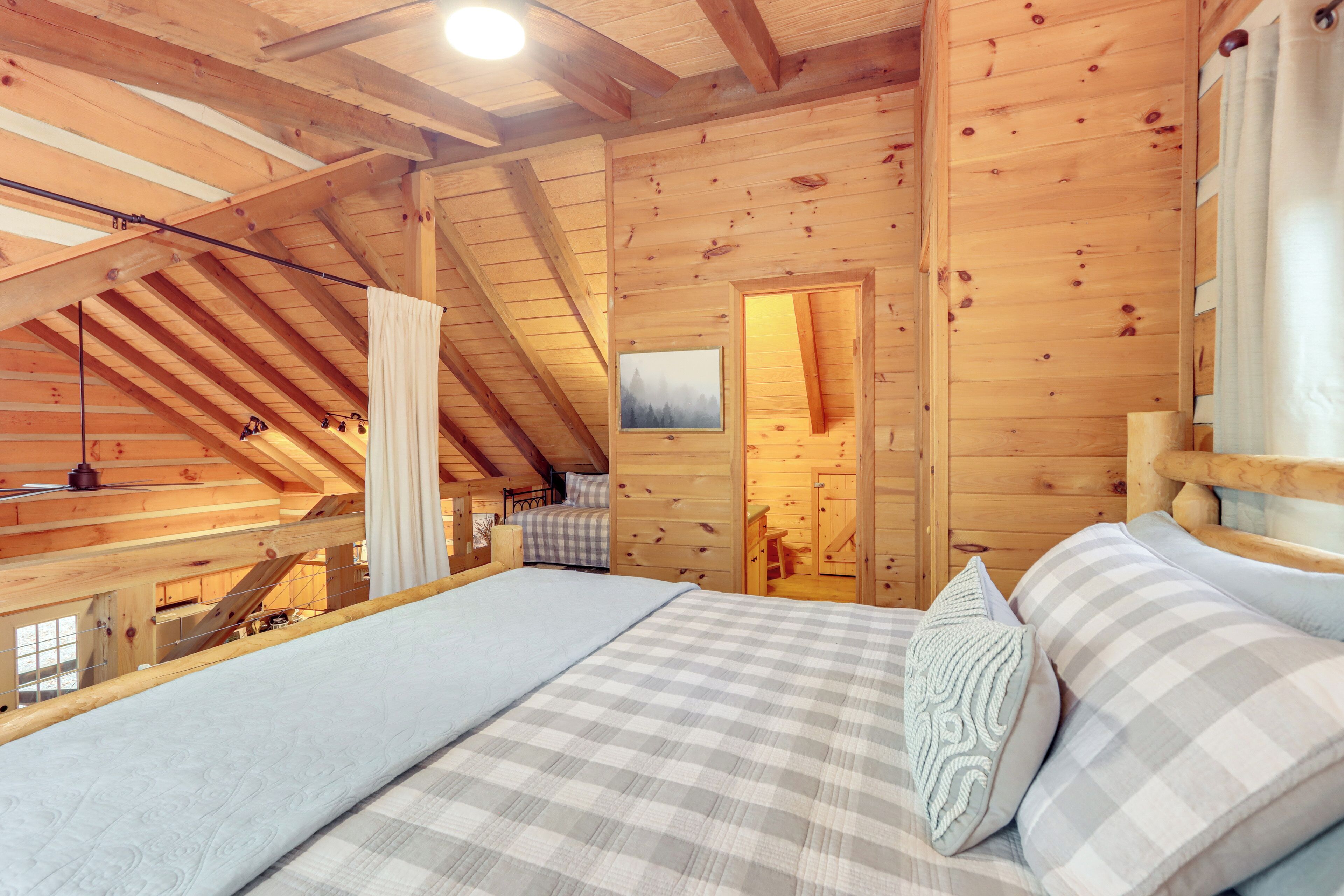 A cozy wooden cabin bedroom with a lofted sleeping area, a bed with checkered bedding, and a painting on the wall.
