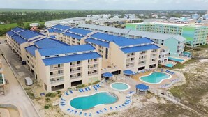 Un hôtel comprenant plusieurs bâtiments, un espace piscine avec des chaises longues et une plage.
