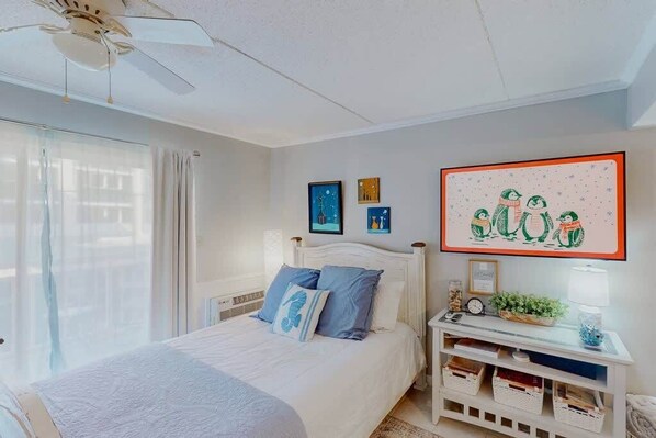 Un dormitorio con cama, ventilador de techo, mesita de noche con lámpara y decoración en la pared.