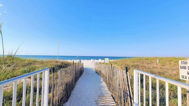Un sentier sablonneux mène à une plage où un panneau indique « ACCÈS À LA PLAGE ».