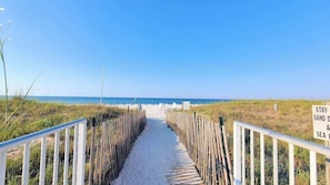 Um caminho de areia que leva a uma praia, com uma placa 'STAY' indicando acesso à praia.