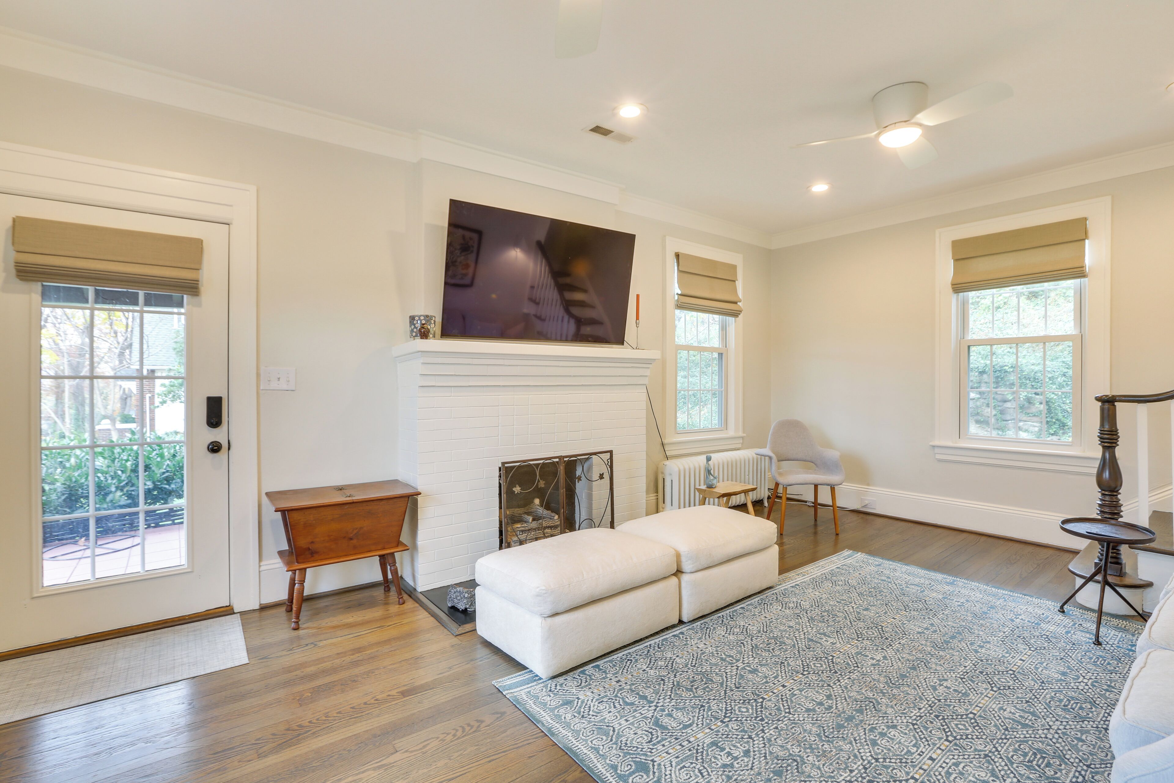 A spacious living room with hardwood flooring, a white fireplace, a large flat-screen TV, and a blue patterned rug.