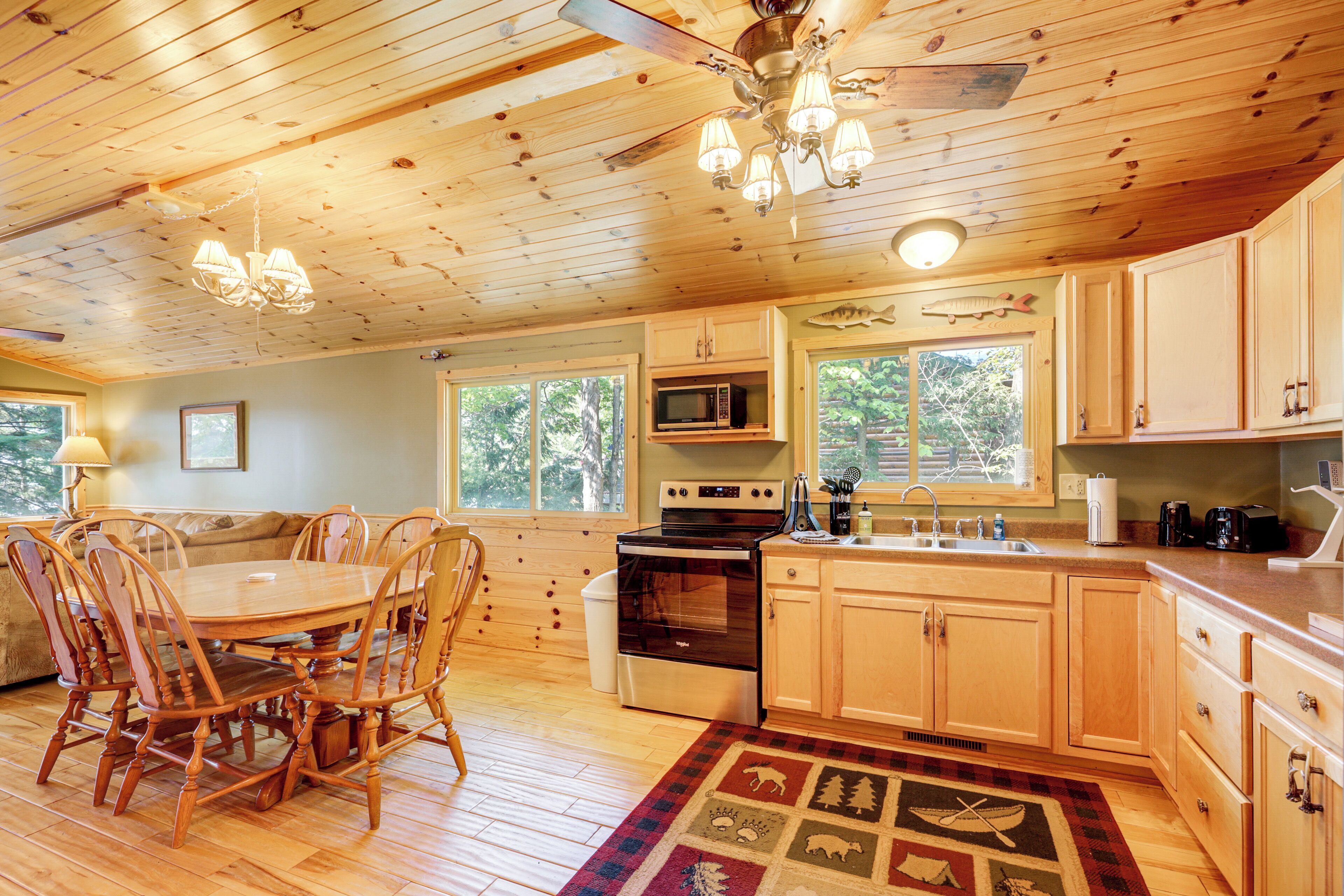 A wooden cabin interior with a dining area, kitchen, and large windows.