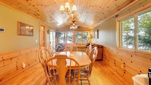 A wooden interior with a dining table and chairs, a ceiling fan, and large windows. - Dock + Fire Pit: Sweet Serenity on Amber Lake (Lac du Flambeau)