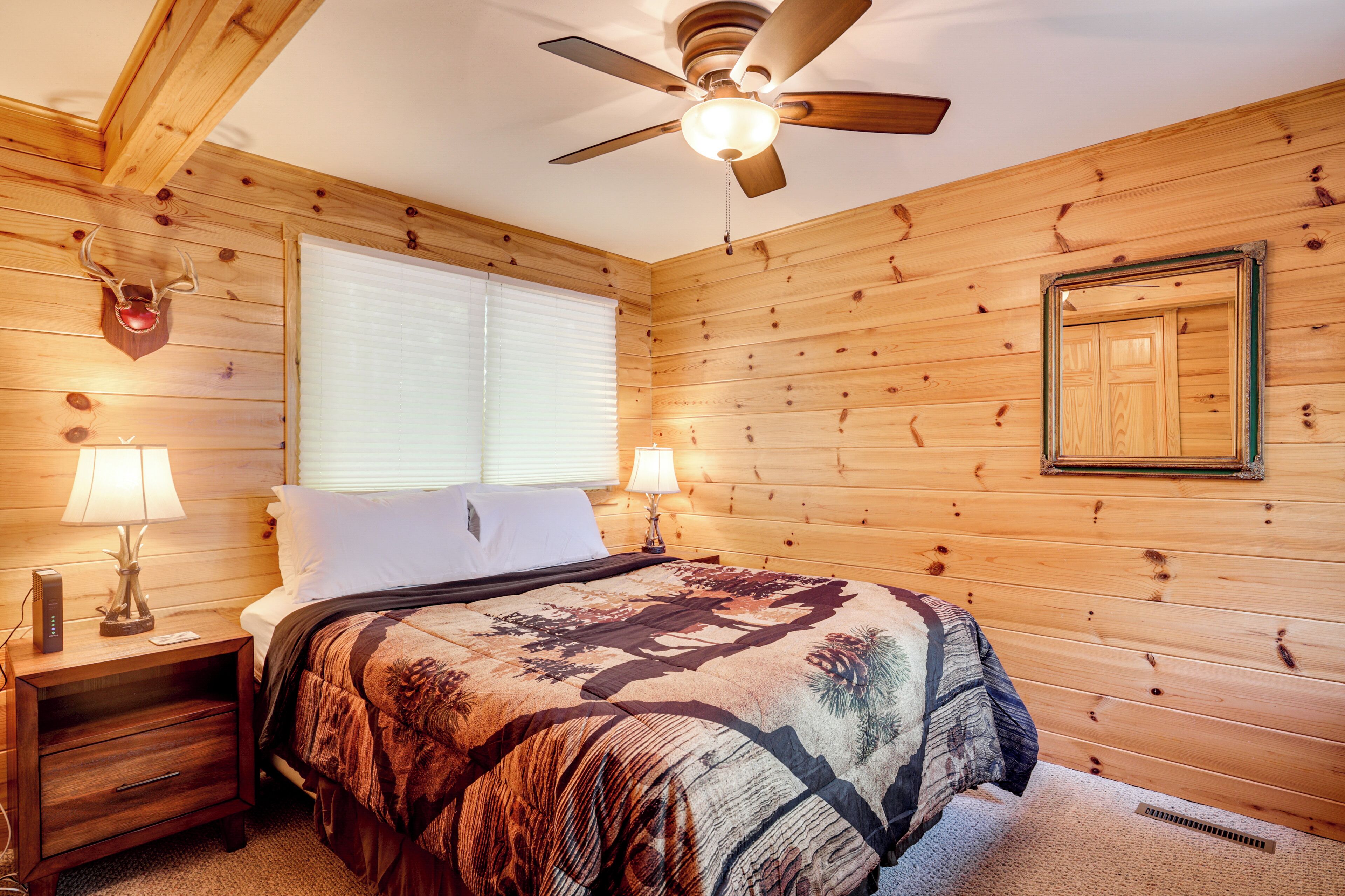 A wooden-paneled bedroom with a bed, two bedside lamps, a ceiling fan, and a window with blinds.