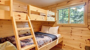 A wooden bunk bed room with a ladder, a window with a view of trees, and a small bedside table. - Dock + Fire Pit: Sweet Serenity on Amber Lake (Lac du Flambeau)