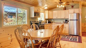 A wooden cabin interior with a dining table, chairs, a refrigerator, and a ceiling fan. - Dock + Fire Pit: Sweet Serenity on Amber Lake (Lac du Flambeau)