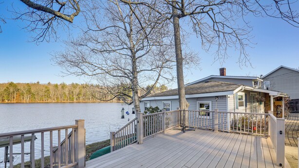 A wooden deck with a railing overlooking a body of water, a house with a chimney, and a clear sky. - Lakefront Salem Retreat - Fish, Swim, Kayak & More (Salem)
