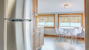 A modern kitchen with a stainless steel refrigerator, wooden cabinets, and a dining area with white chairs and a table. - Lakefront Salem Retreat - Fish, Swim, Kayak & More (Salem)