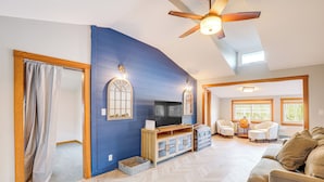 A spacious living room with a large TV, wooden entertainment unit, and a ceiling fan. - Lakefront Salem Retreat - Fish, Swim, Kayak & More (Salem)