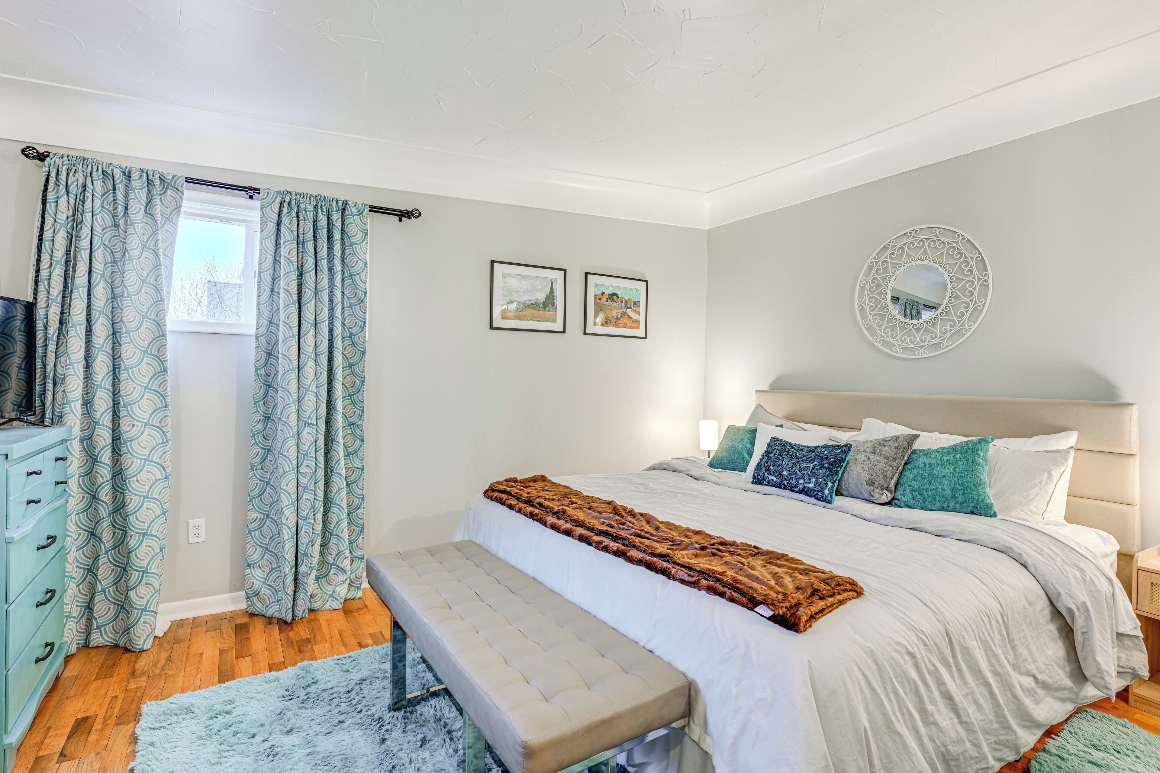 Un dormitorio con cama, banco, cómoda y dos cuadros en la pared.