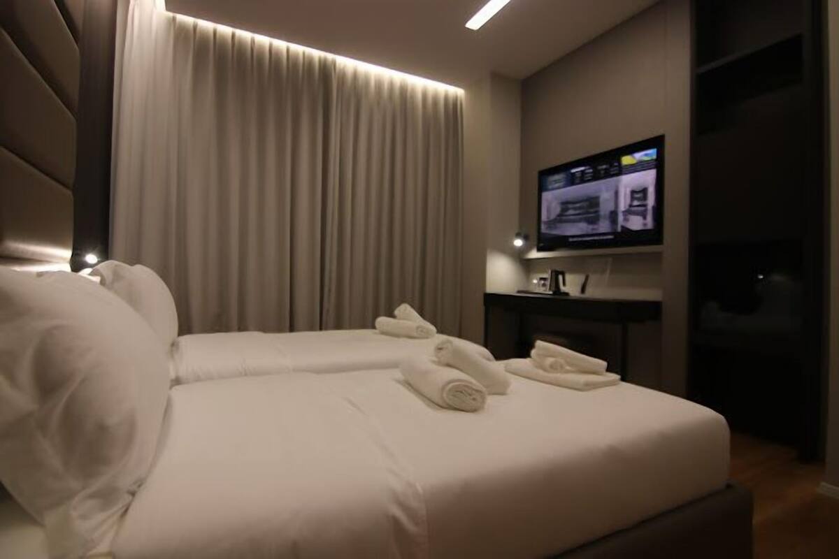 A hotel room with a large bed, a flat-screen TV mounted on the wall, and a curtain.